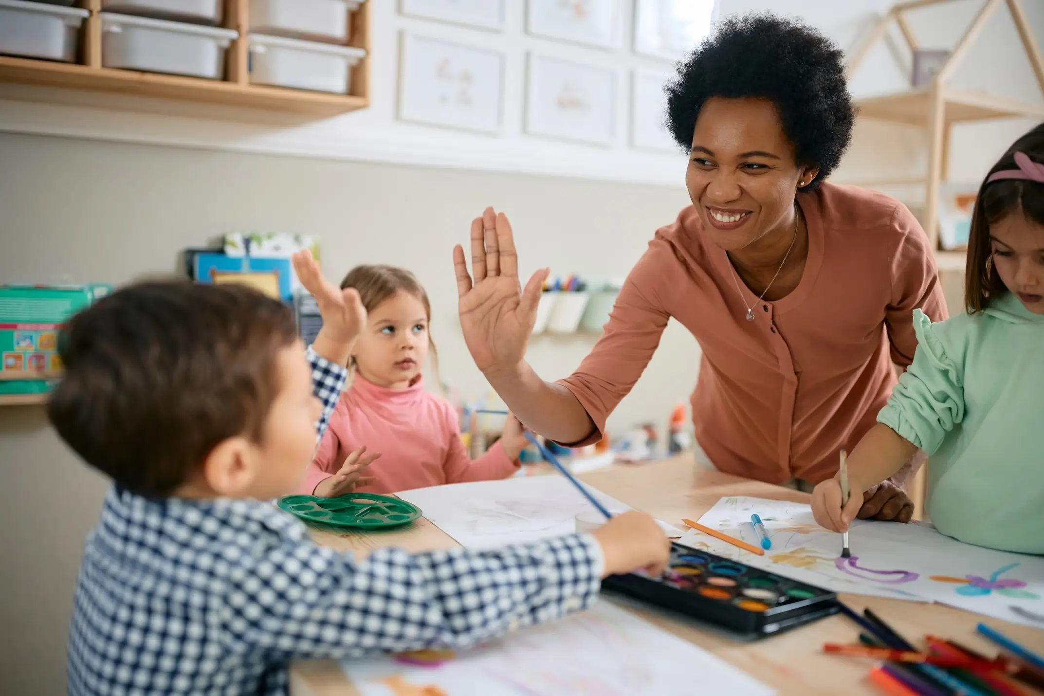 An early childhood educator gives a high-five to her preschool student
